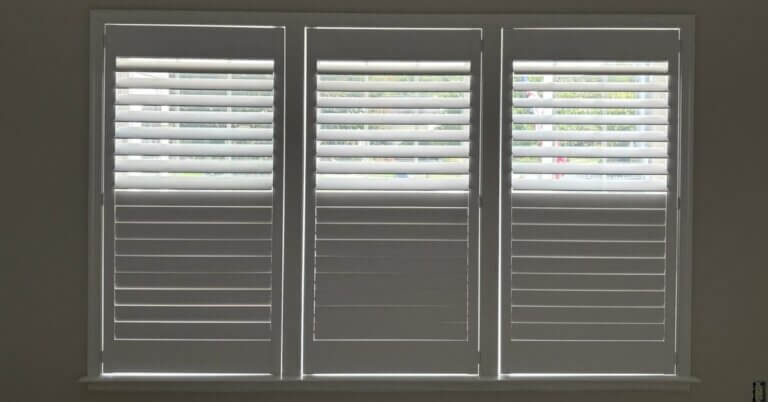 Custom white wood plantation shutters on residential windows in Millsboro, with louvers partially open for natural light.